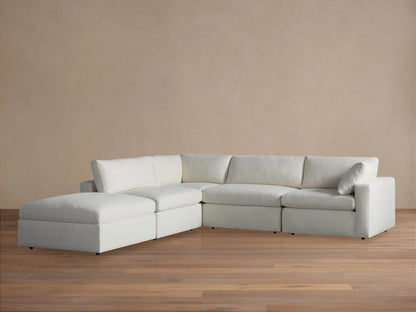 L-shaped Beale Five Piece Sectional in off-white fabric with plush, deep cushions & a left-side chaise, against a light brown wall.