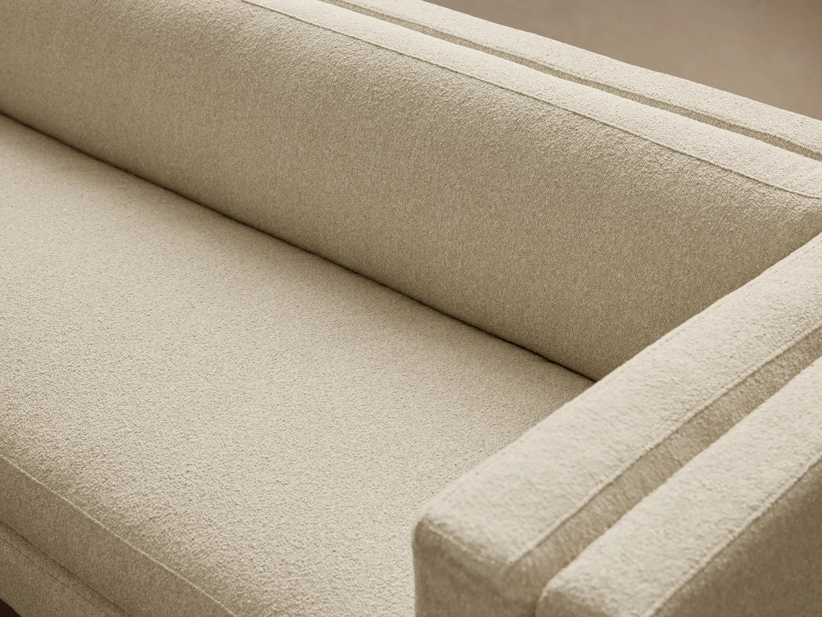 Light beige modern textured fabric sofa with a low back, subtly recessed arms, and slender gold legs, on a wood floor.