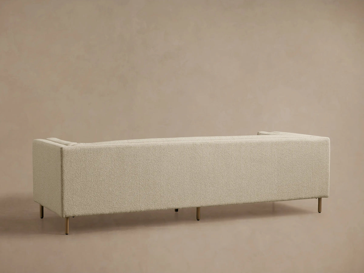 Angled close-up of a cream-colored boucle-style textured fabric sofa, showing armrest, seat, and back cushions.