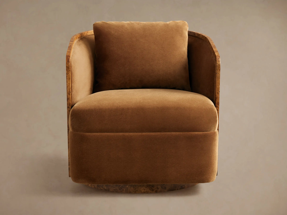 Tilda Swivel Chair with a rounded, modern design, upholstered in rich caramel velvet. Features a curved, exposed burlwood frame and matching pillow.