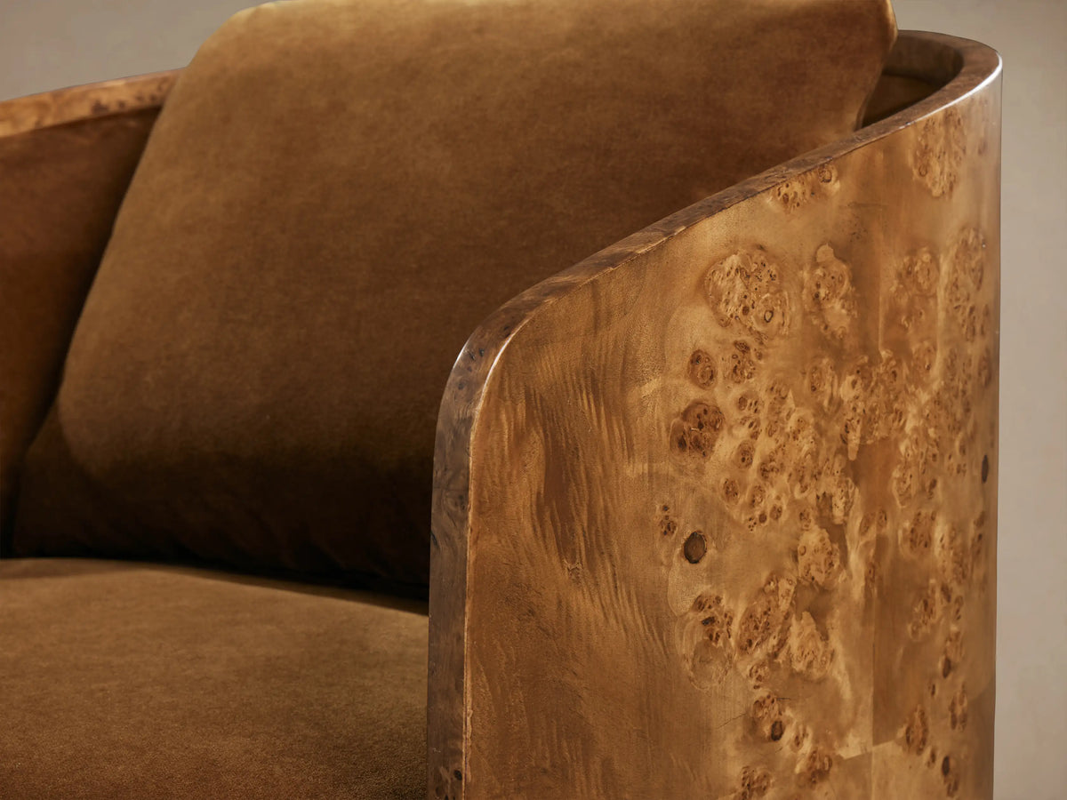 Close-up of Tilda Swivel Chair with curved burl wood frame featuring unique grain, and plush, warm brown upholstery.