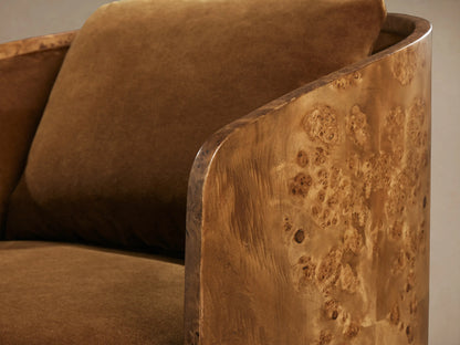 Close-up of Tilda Swivel Chair with curved burl wood frame featuring unique grain, and plush, warm brown upholstery.