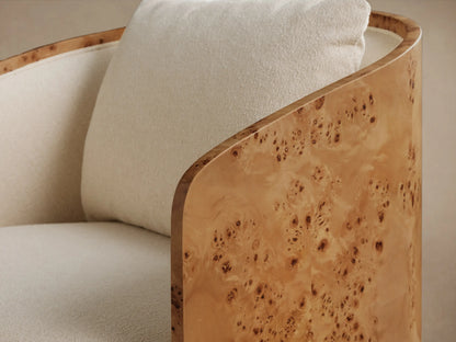 Close-up of Tilda Swivel Chair with curved, light brown burl wood frame and cream bouclé fabric upholstery, including a pillow.