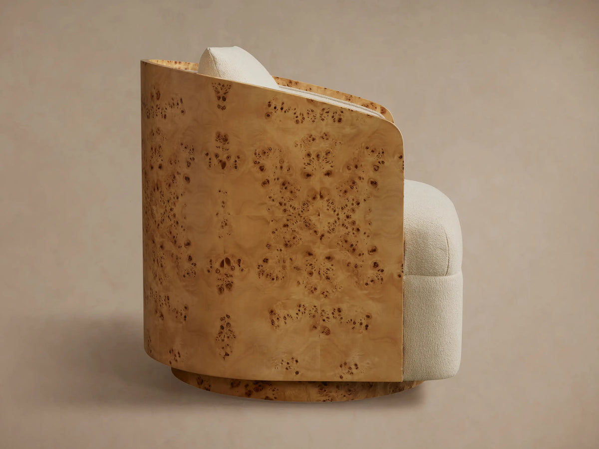 Side view of Tilda Swivel Chair with curved burl wood exterior and light cream textured fabric upholstery, including a pillow.