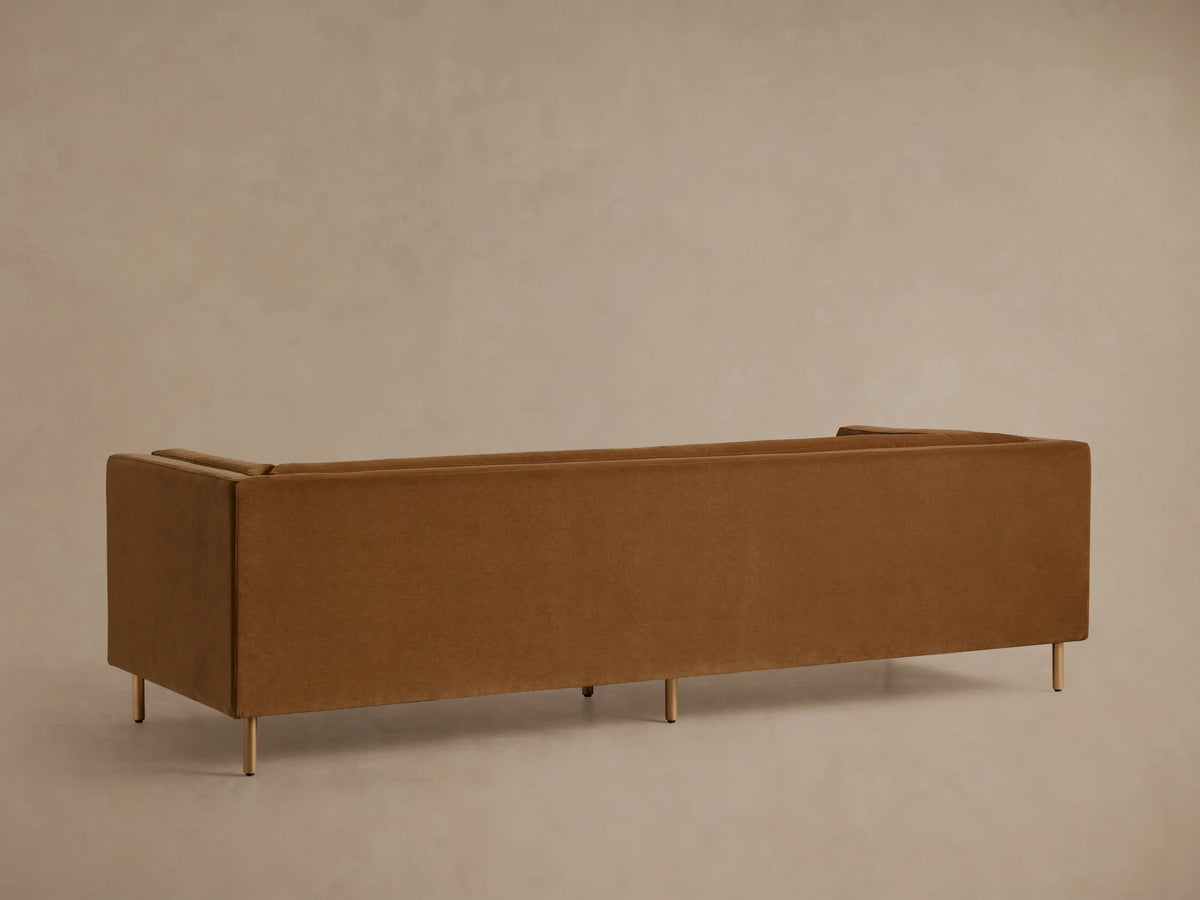 Angled close-up of a warm brown plush upholstered sofa, showing two distinct cushions with subtle seam lines.