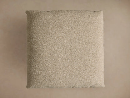 Deacon Ottoman with a textured beige cushion on a round, brushed bronze metal base, showcasing a modern design.
