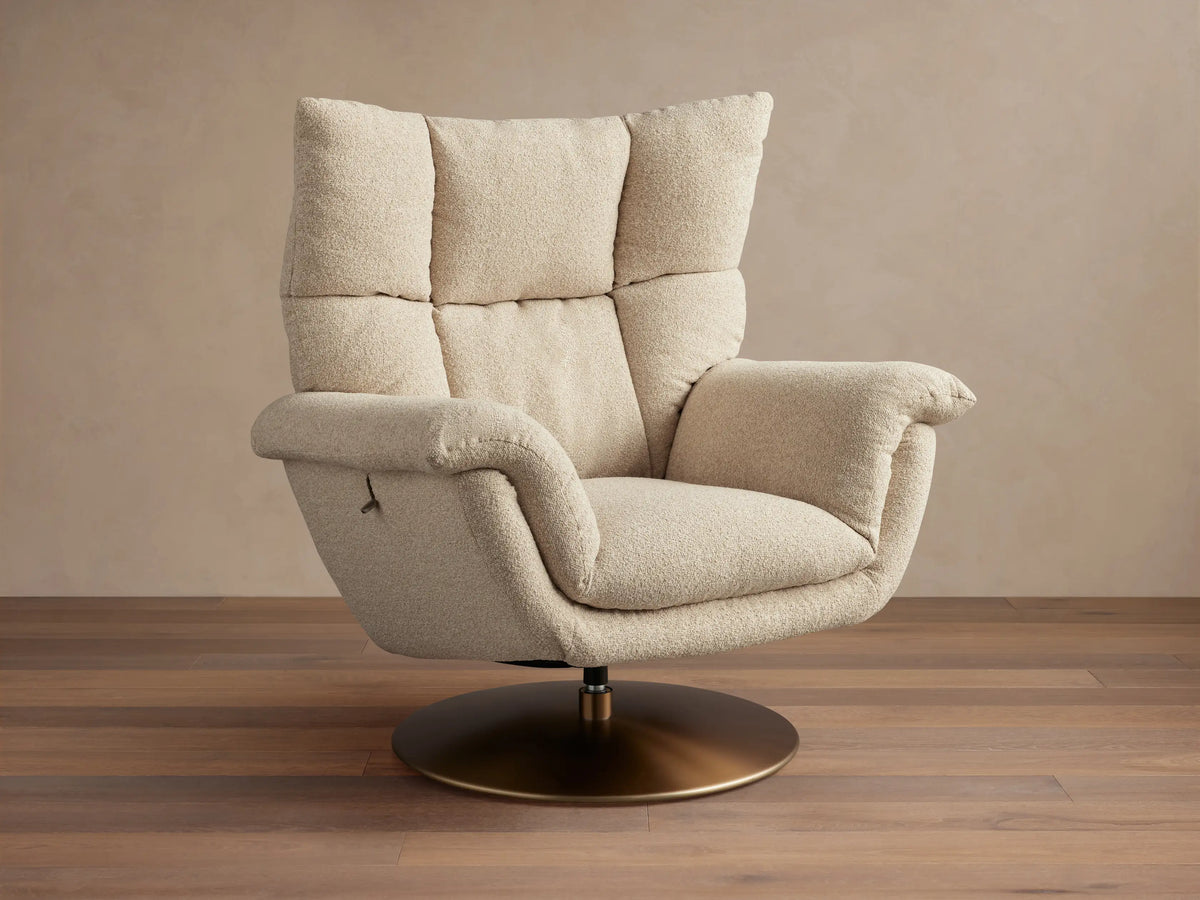 Deacon Swivel Recliner in beige fabric, with high cushioned backrest, curved armrests, and a bronze swivel base on wooden floor.