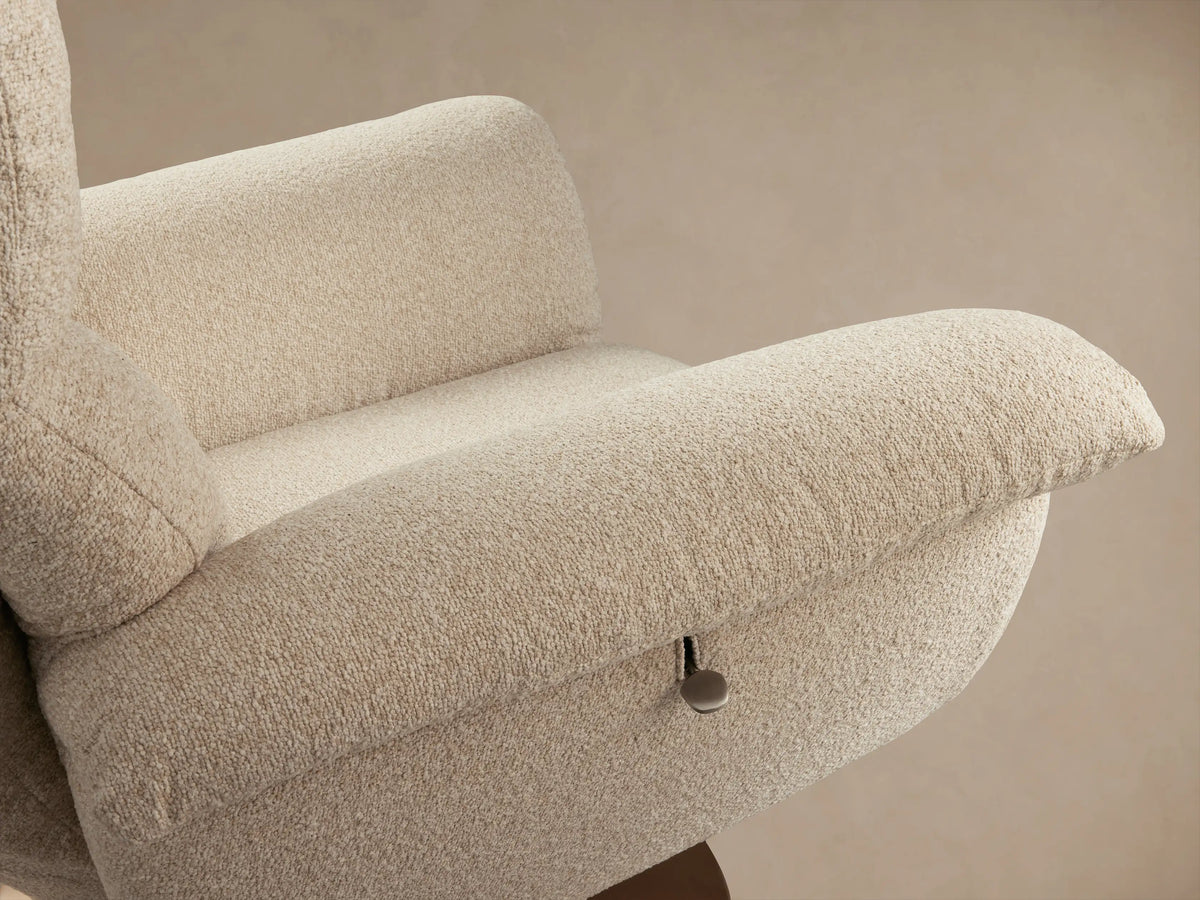 Deacon Swivel Recliner in soft beige fabric, wide padded arms, high backrest, on a bronze-toned swivel base, on wood floor.