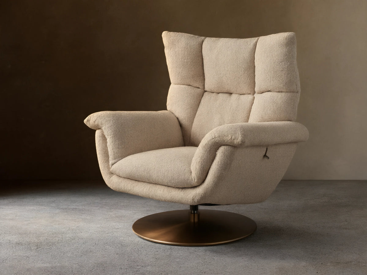 Deacon Swivel Recliner in beige fabric, with high cushioned backrest, curved armrests, and a bronze swivel base on wooden floor.