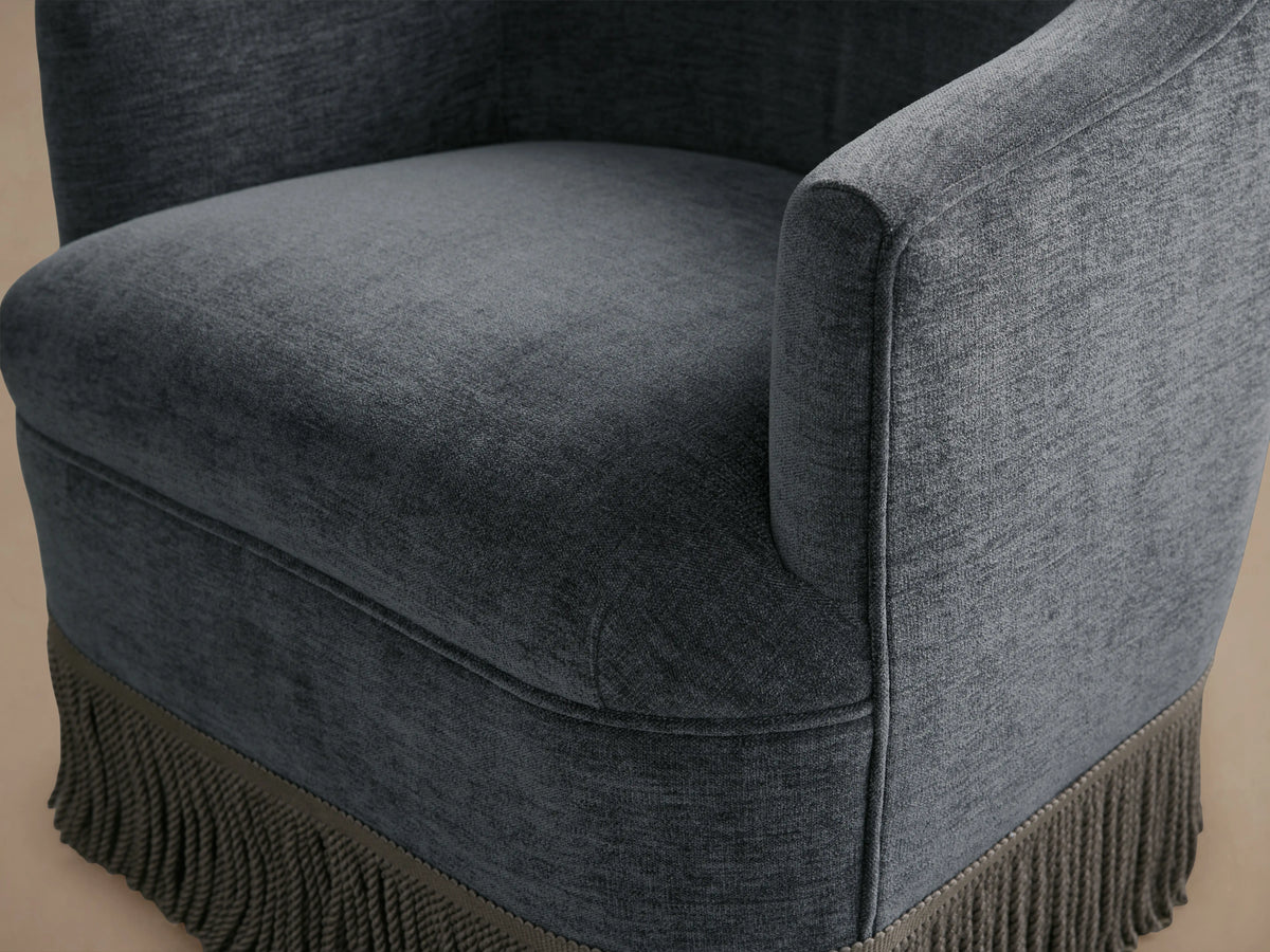 Dark gray Savannah Swivel Chair with a comfortable cushioned seat and back, featuring fringe detail at the base, on wooden flooring.
