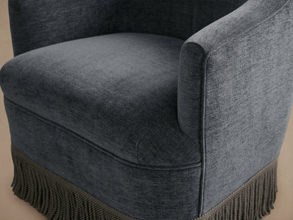 Dark gray Savannah Swivel Chair with a comfortable cushioned seat and back, featuring fringe detail at the base, on wooden flooring.
