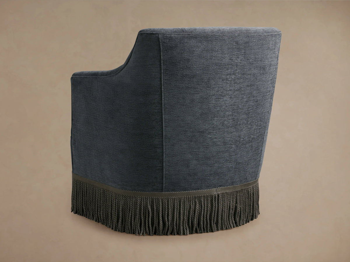 Savannah Swivel Chair in dark gray fabric with fringe detailing at the base, featuring a curved backrest and armrest design.