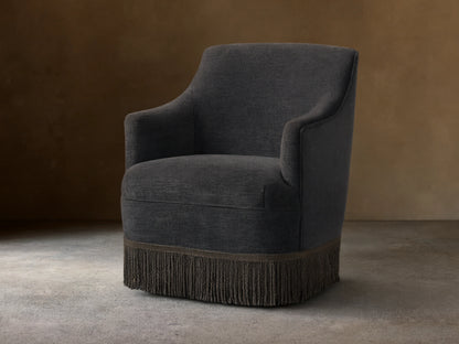 Savannah Swivel Chair in dark gray fabric, featuring a rounded back, sleek armrests, and a decorative fringe at the base.
