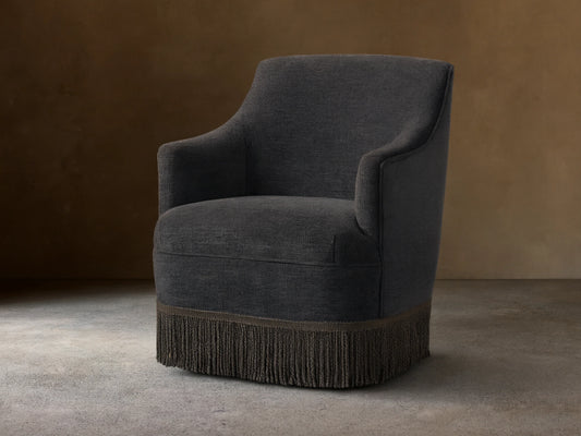 Savannah Swivel Chair in dark gray fabric, featuring a rounded back, sleek armrests, and a decorative fringe at the base.