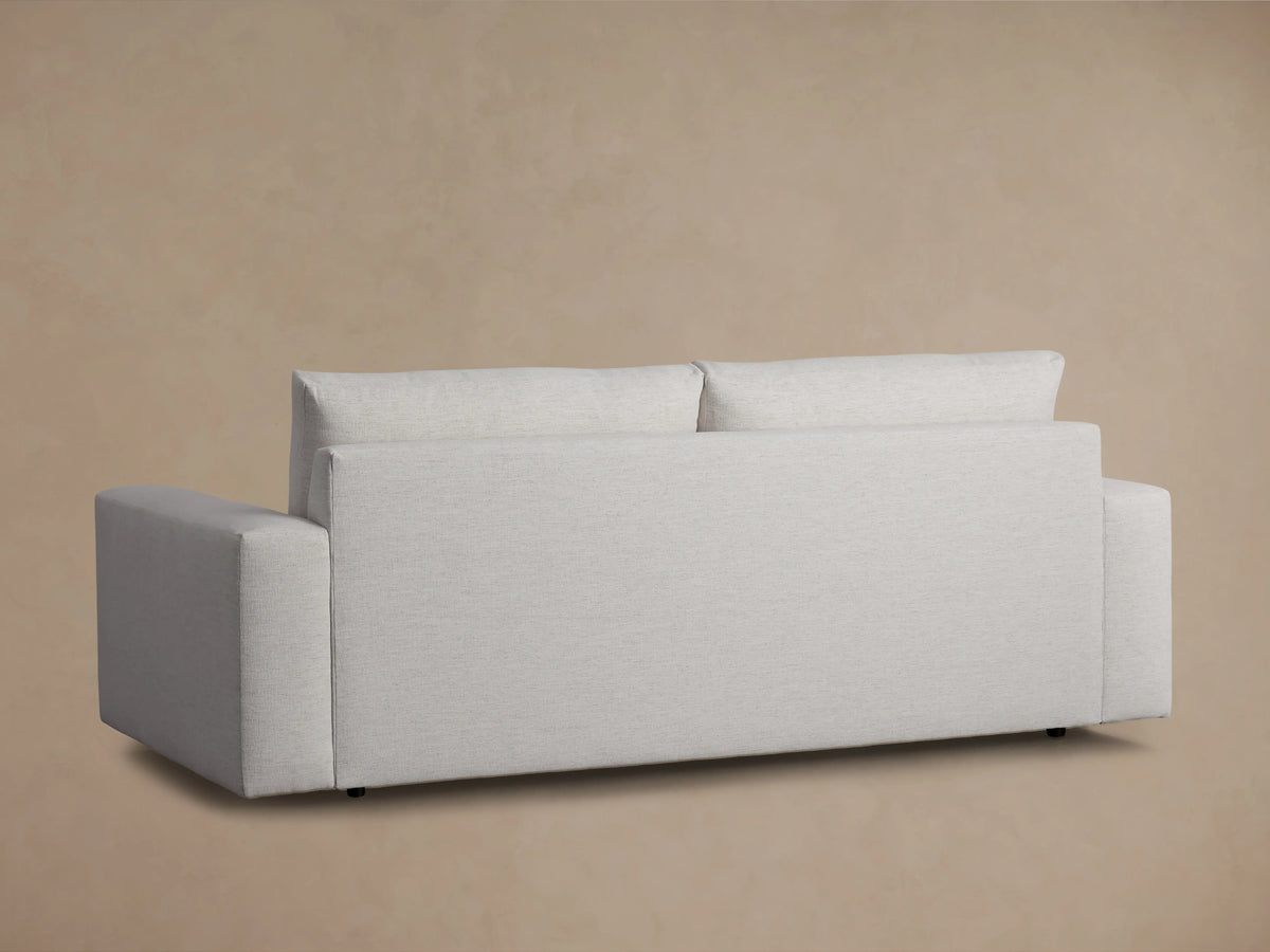 Kipton Wide Arm Sofa in light gray fabric, viewed from the back with broad armrests and a high backrest, against a beige background.
