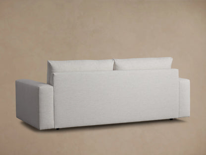 Kipton Wide Arm Sofa in light gray fabric, viewed from the back with broad armrests and a high backrest, against a beige background.