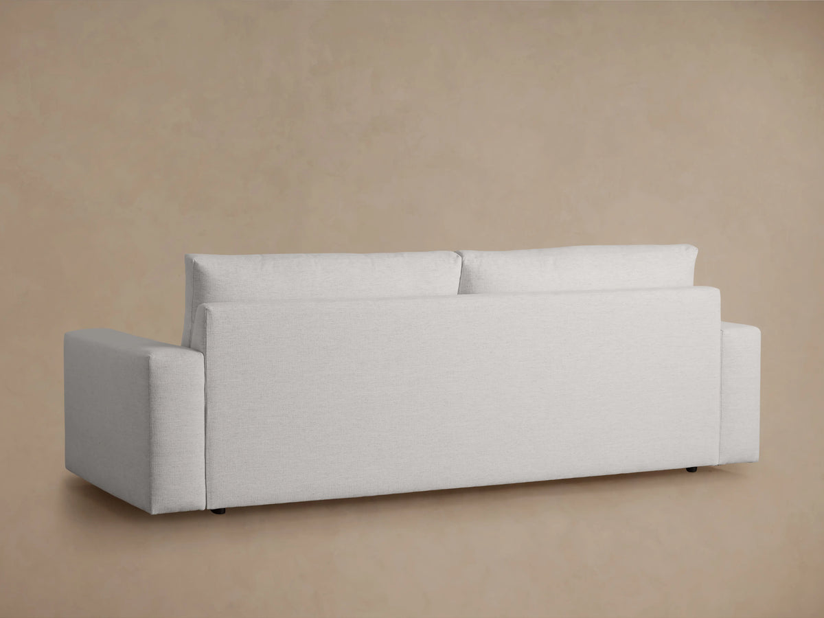 Kipton Wide Arm Sofa in light gray fabric, viewed from the back. Features wide armrests and minimalist design against a beige background.