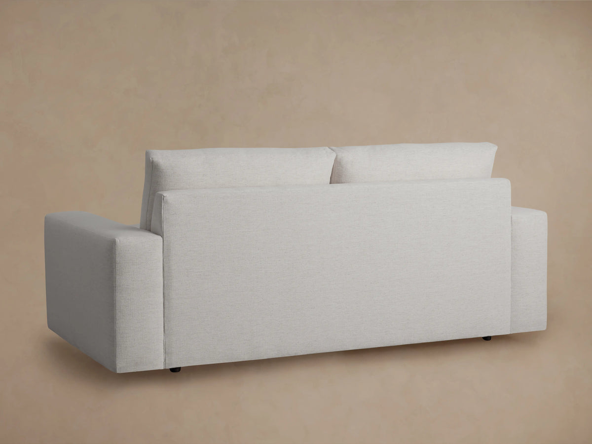Kipton Wide Arm Sofa in light gray fabric with plush seat and back cushions, wide arms, on a wooden floor, beige wall behind.