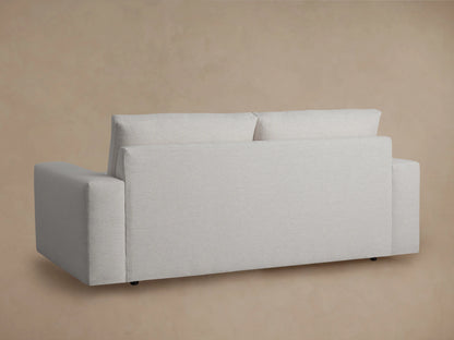 Kipton Wide Arm Sofa in light gray fabric with plush seat and back cushions, wide arms, on a wooden floor, beige wall behind.