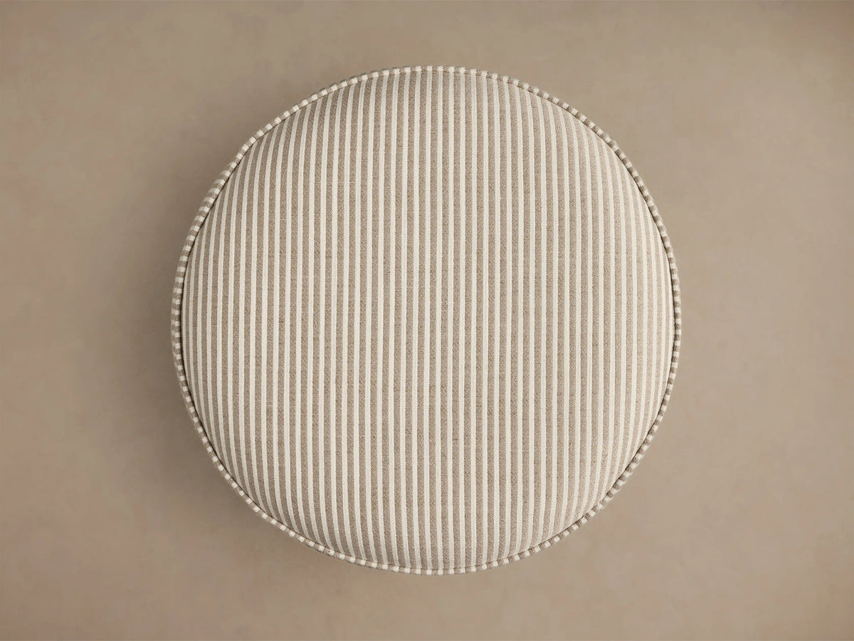Top-down view of the round beige and white striped upholstered Mimi Ottoman, featuring prominent piping around the edge.