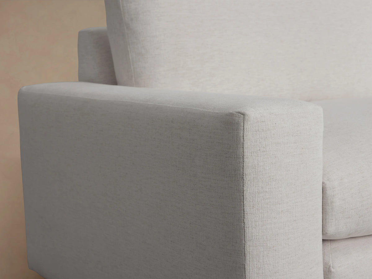 Wide arm sofa upholstered in light gray fabric, featuring two large back cushions and seat cushions. Placed on wooden floor with beige wall background.