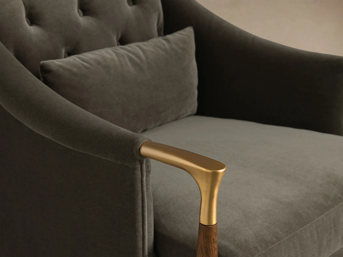 Close-up of the dark gray velvet Fisher Club Chair, with its tufted back, lighter gray lumbar pillow, and brass and wood arm.