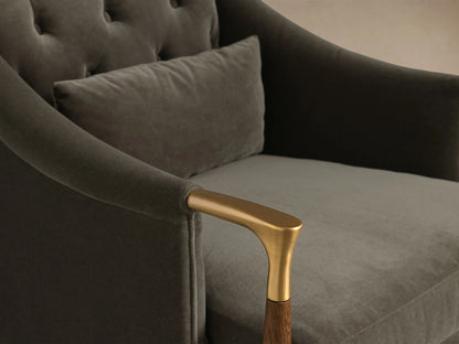 Close-up of the dark gray velvet Fisher Club Chair, with its tufted back, lighter gray lumbar pillow, and brass and wood arm.