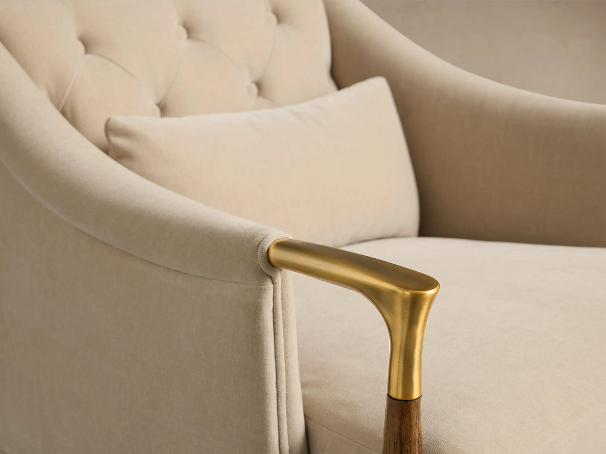 Detail view of the beige Fisher Club Chair, showing a tufted back, matching lumbar pillow, and a brass armrest with wood accent.