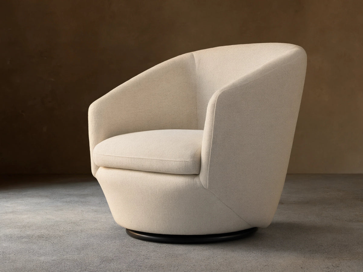 Swivel chair with light beige fabric, curved armrests, cushioned seat and backrest on a black circular base, sitting on wood floor.