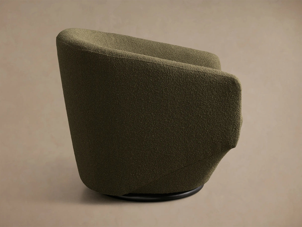 Side profile of the olive green Pelton Swivel Chair, showing its textured fabric and black circular swivel base.