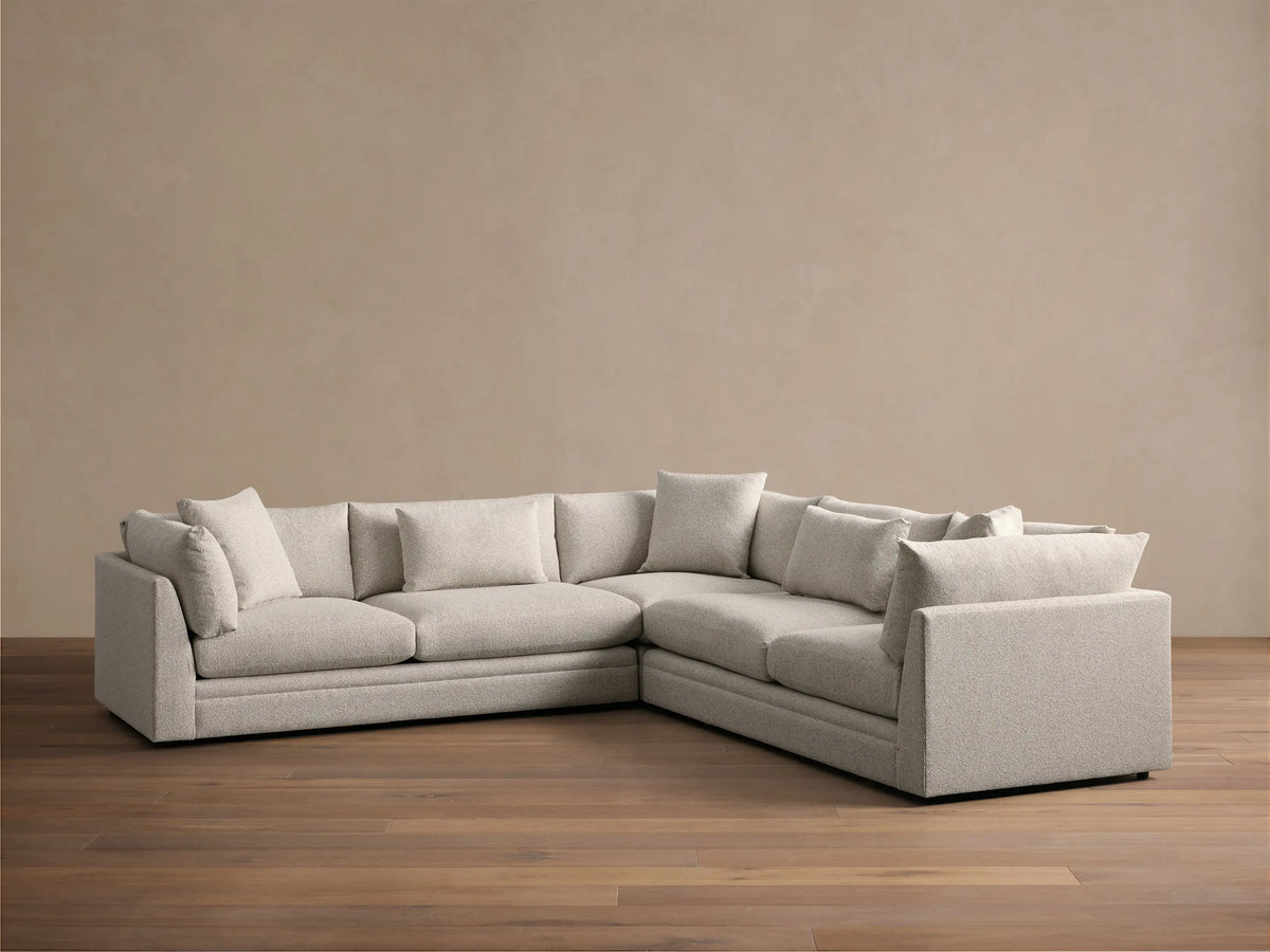 Light grey textured Pavo Three Piece Corner Sectional sofa, L-shaped, with multiple cushions, on a wood floor.
