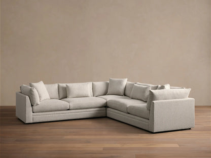 Light grey textured Pavo Three Piece Corner Sectional sofa, L-shaped, with multiple cushions, on a wood floor.