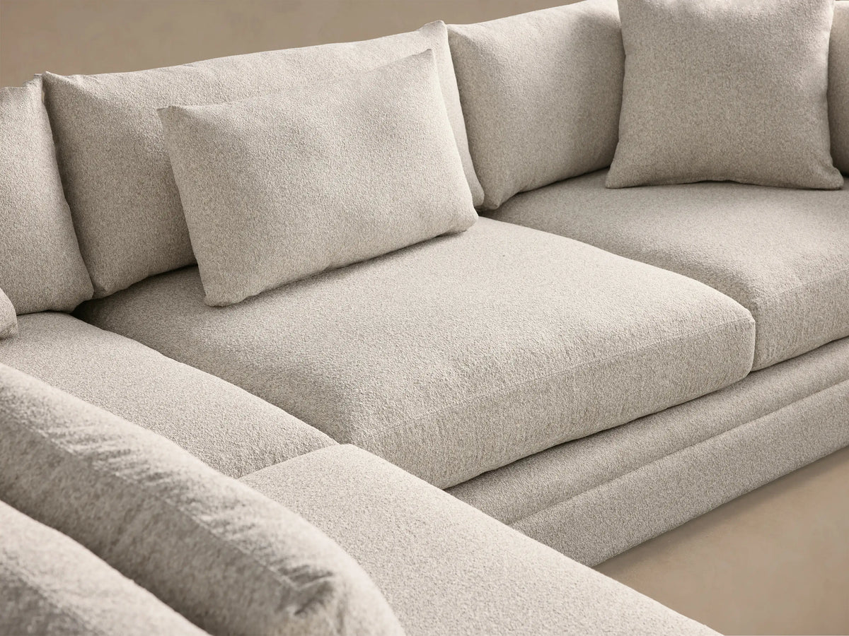 Light grey Pavo Three Piece Corner Sectional, L-shaped, with plush cushions, on a wooden floor against a tan wall.