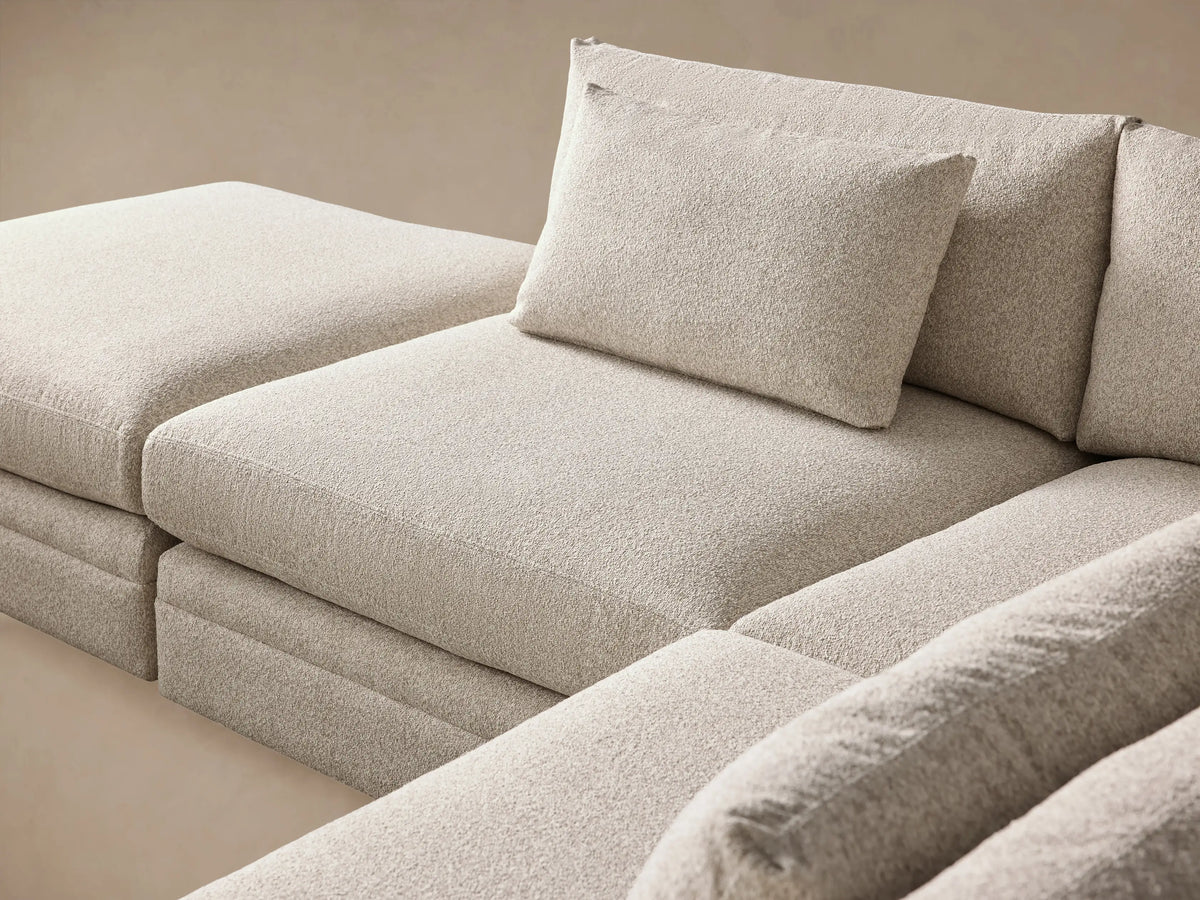 Pavo L-shaped sectional in light beige textured fabric, with deep plush cushions & throw pillows, on a wood floor.