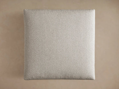 Close-up of a light gray, textured Pavo Ottoman, showing its plush top cushion resting on the upholstered base.