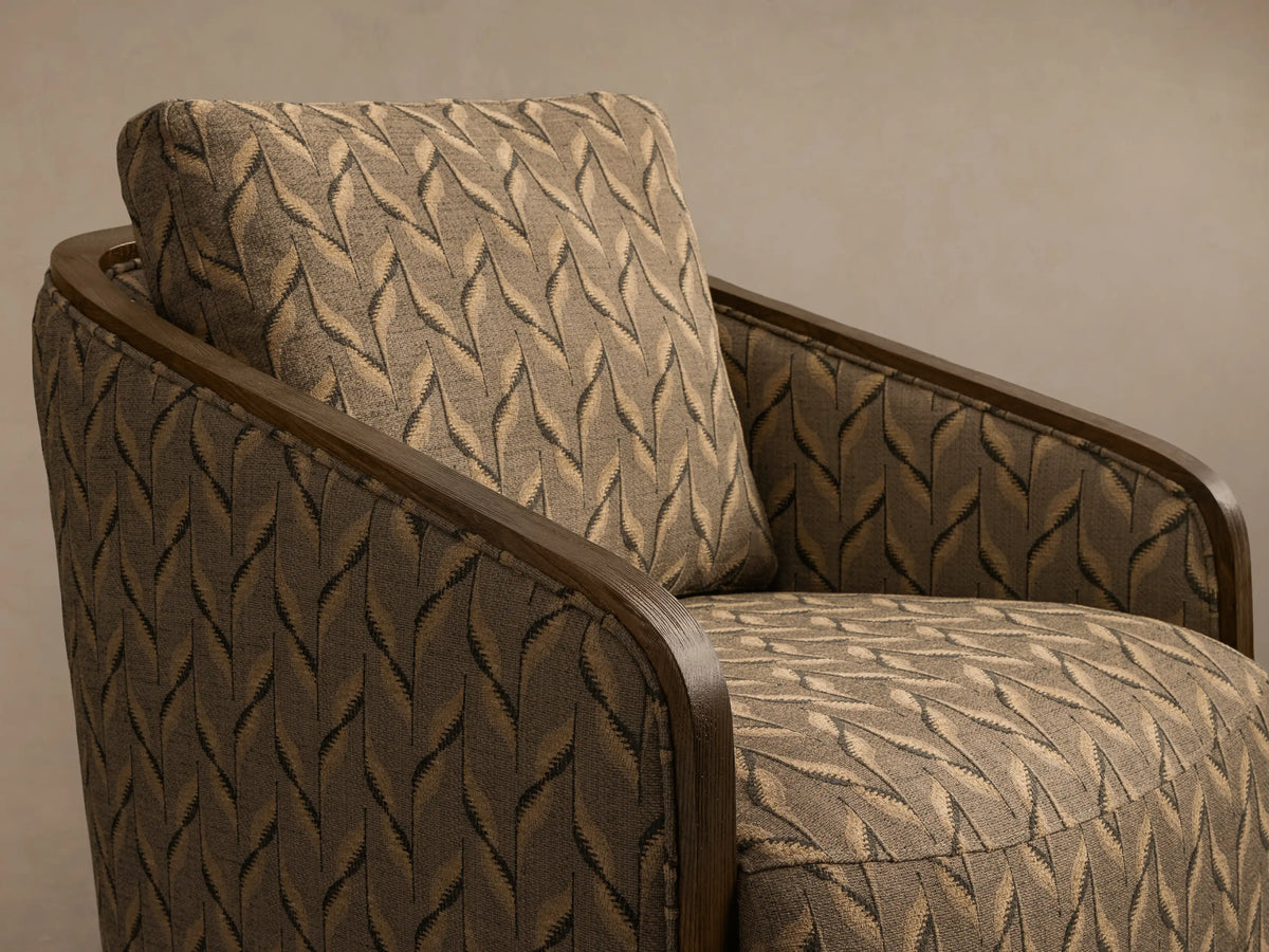 Front view of the Pomona Swivel Chair upholstered in a beige and brown leaf-like geometric pattern with exposed oak arms and swivel base.