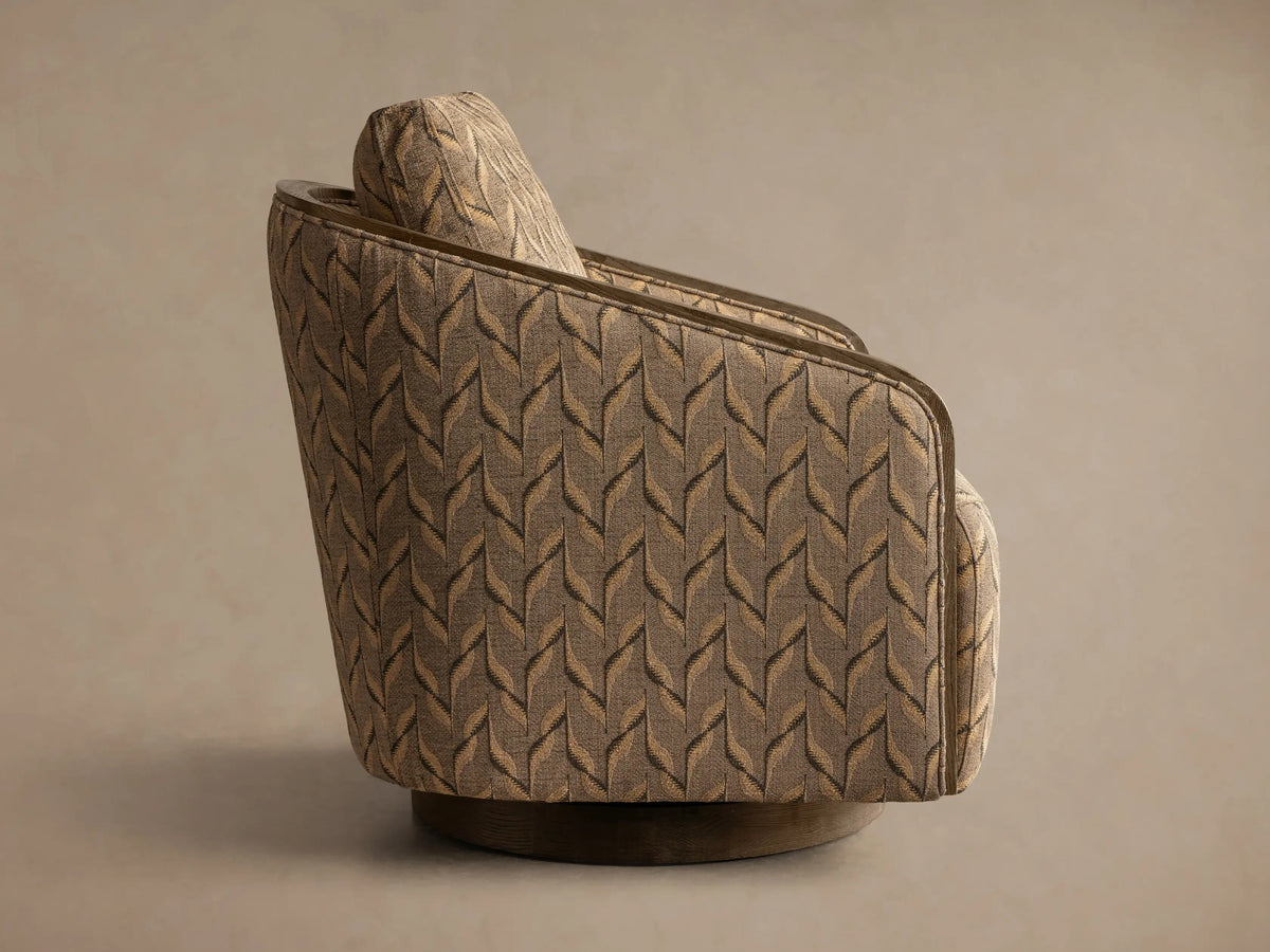 Rear view of the Pomona Swivel Chair, upholstered in a brown and beige leaf patterned fabric, with an exposed oak trim and dark wood swivel base.