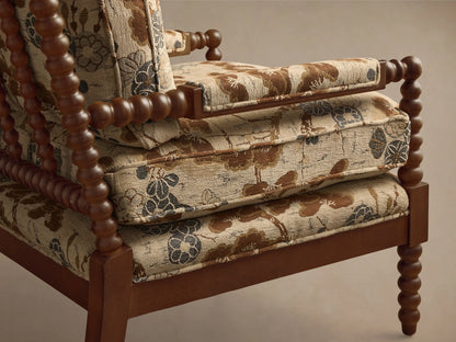 Close-up, angled view of the Milly Chair, featuring its brown spindled wood frame and beige upholstery with brown and blue floral pattern.