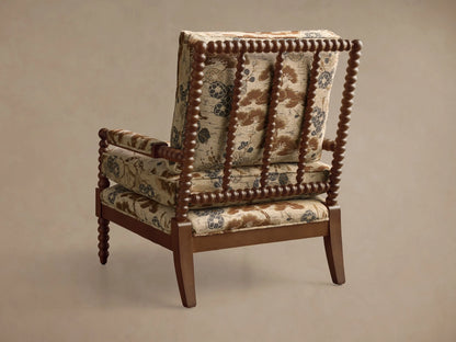 Rear 3/4 view of the Milly Chair. Dark wood frame with spindled details, and beige patterned upholstery with brown and blue florals.