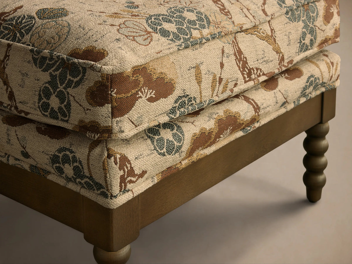 Beige, brown, and blue nature-patterned Milly Ottoman with a light brown wooden frame and turned legs.