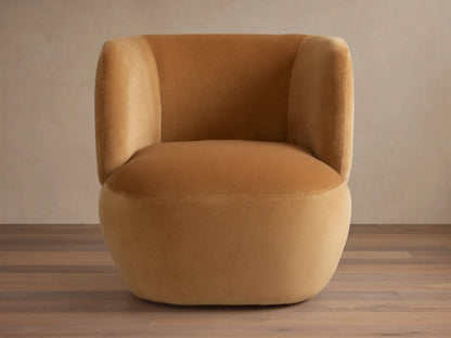 Lenny Swivel Chair in caramel brown fabric with a rounded seat, curved backrest, stout arms, and smooth upholstery on wooden floor.