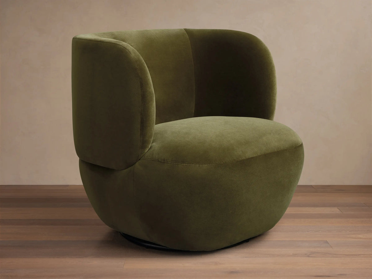 Olive green velvet upholstered chair featuring a deeply curved back and integrated armrests.