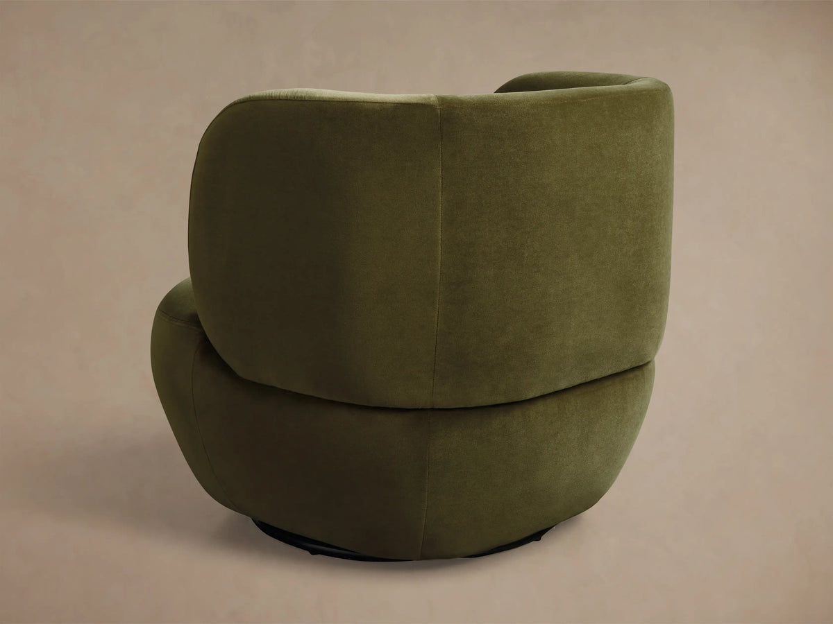 Close-up of green velvet armchair, highlighting the curved backrest and armrest with soft, plush fabric.