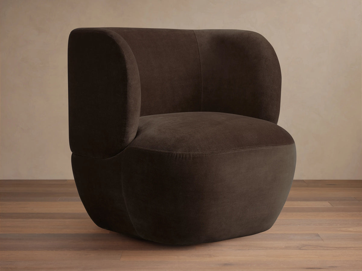 Dark brown Lenny Swivel Chair with plush, rounded backrest and seat, set on a wooden floor. The chair features a seamless, modern design.