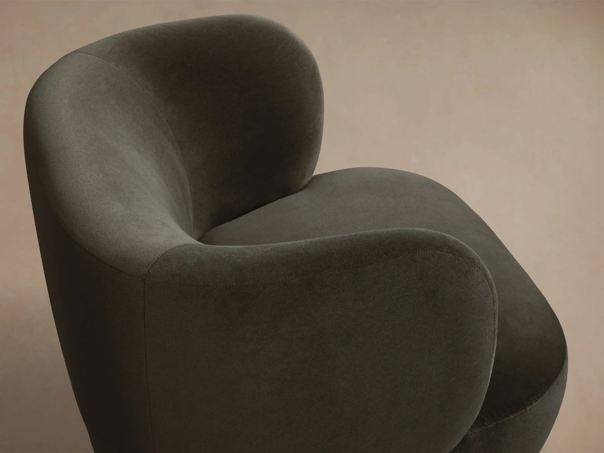 Front view of a dark green velvet armchair with a rounded, sculptural shape and plush texture.