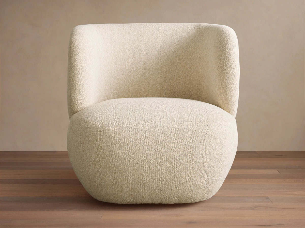 Lenny Swivel Chair, modern, full-bodied, light cream textured fabric with curved back and arms, on a wooden floor.