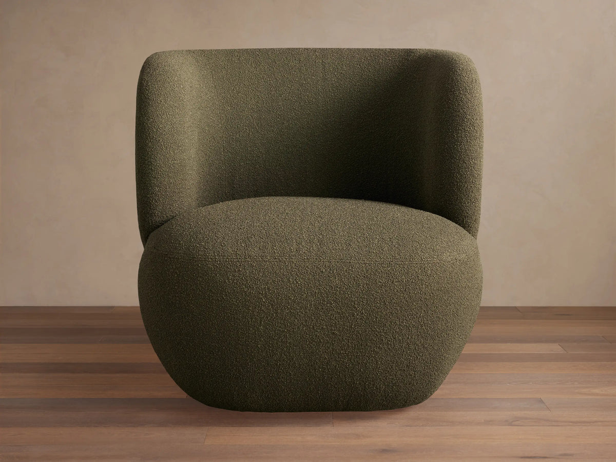 Lenny Swivel Chair: Plump dark green boucle chair with curved back, wide arms, and a solid base, on a wooden floor.