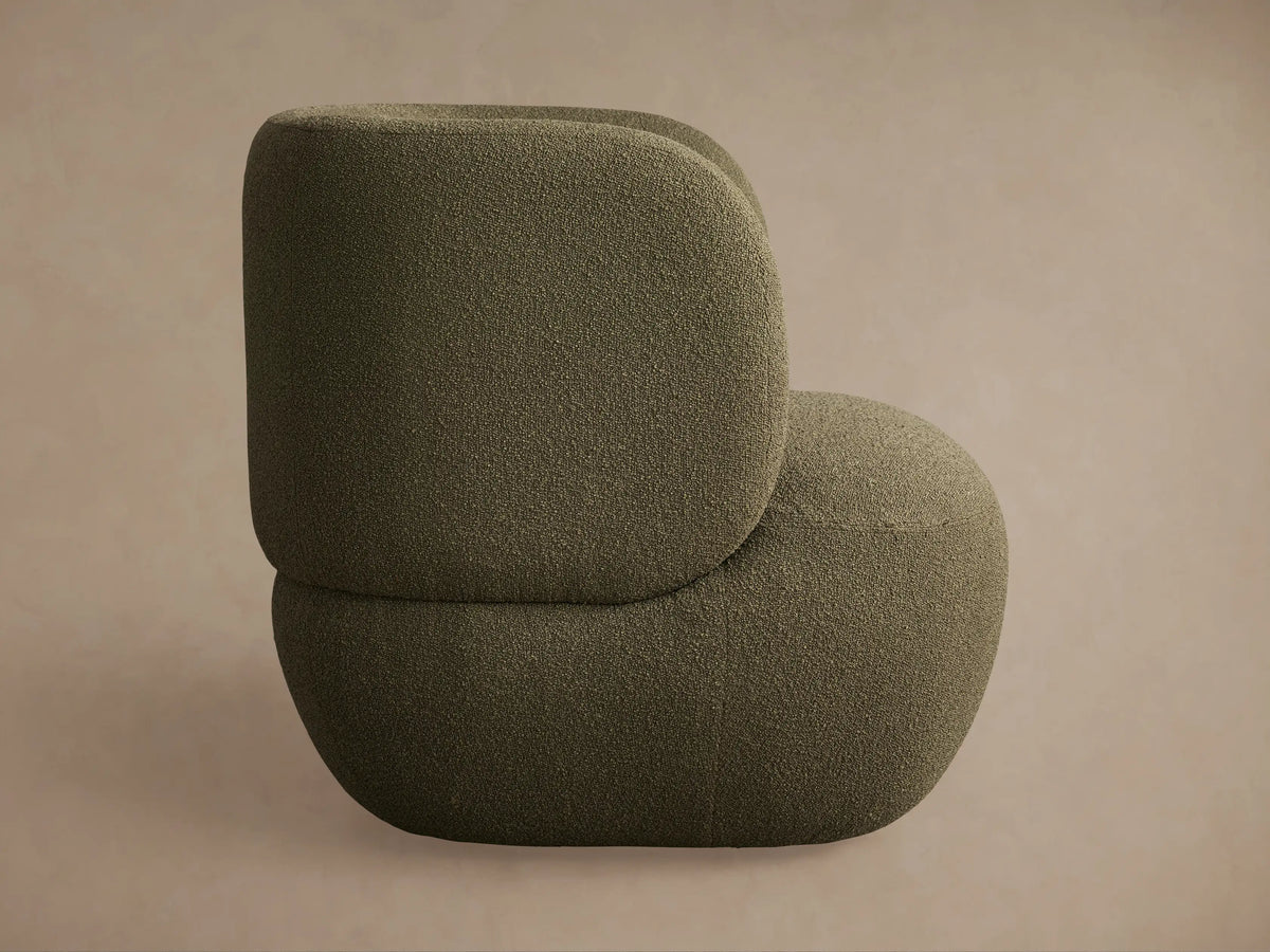 Back view of a dark olive green Lenny Swivel Chair, featuring a rounded, plush shape and textured fabric against a neutral beige wall.