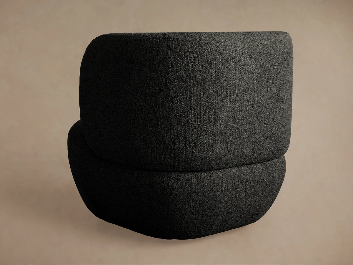 Close-up of Lenny Swivel Chair's dark grey, boucl??-like textured fabric upholstery, highlighting a gentle curve.
