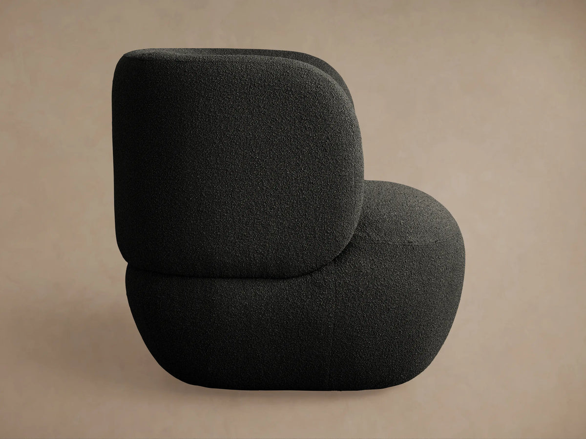 Modern black Lenny Swivel Chair with textured fabric, featuring a rounded back and seat, viewed slightly from the front against a tan wall.